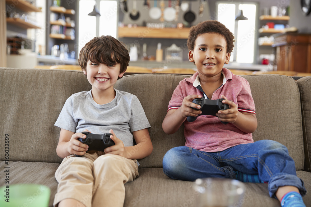 Obraz premium Two Boys Sitting On Sofa In Lounge Playing Video Game Together