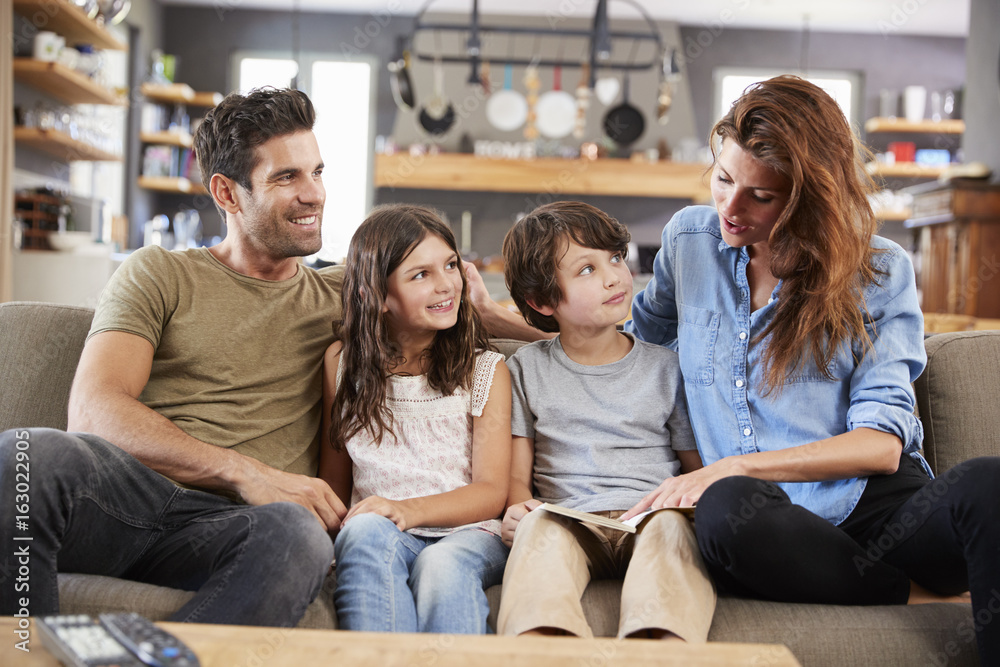 Family Sitting On Sofa In Lounge Reading Book Together Family Sitting On Sofa In Lounge Reading Book Together