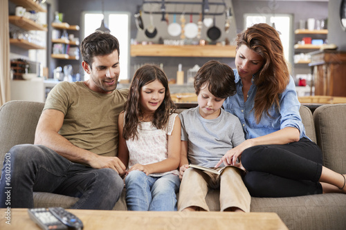 Family Sitting On Sofa In Lounge Reading Book Together