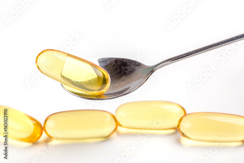 Close up a soft gel capsules on spoon with blurred another capsules in background, essential oil supplement intake concept.