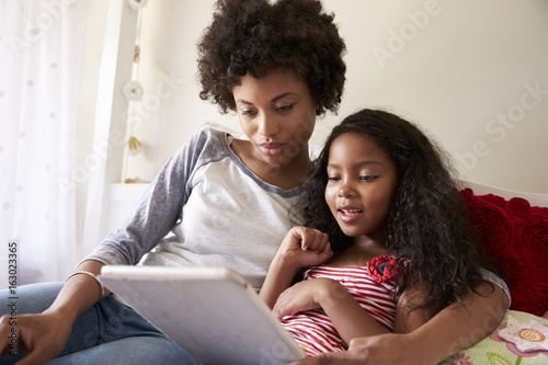 Mother And Daughter Siting On Bed Using Digital Tablet