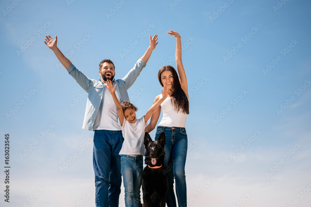 Happy young family standing together with dog and smiling at camera outdoors