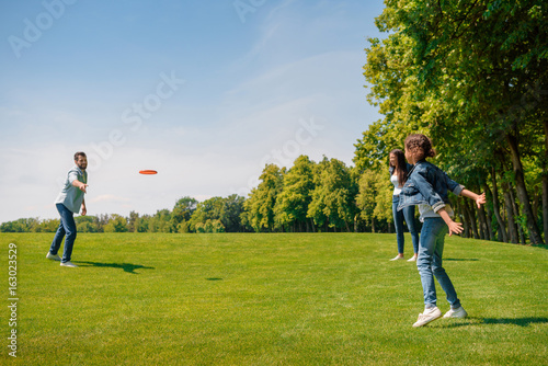 Happy parents with daughter playing with flying disk on green grass