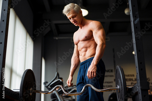 Strong man with muscular body working out in gym. Weight exercise with barbell in fitness club.