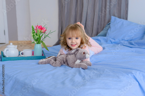 cute girl in pajamas lying on her bed with her favorite toy the rabbit after Sunday's Breakfast