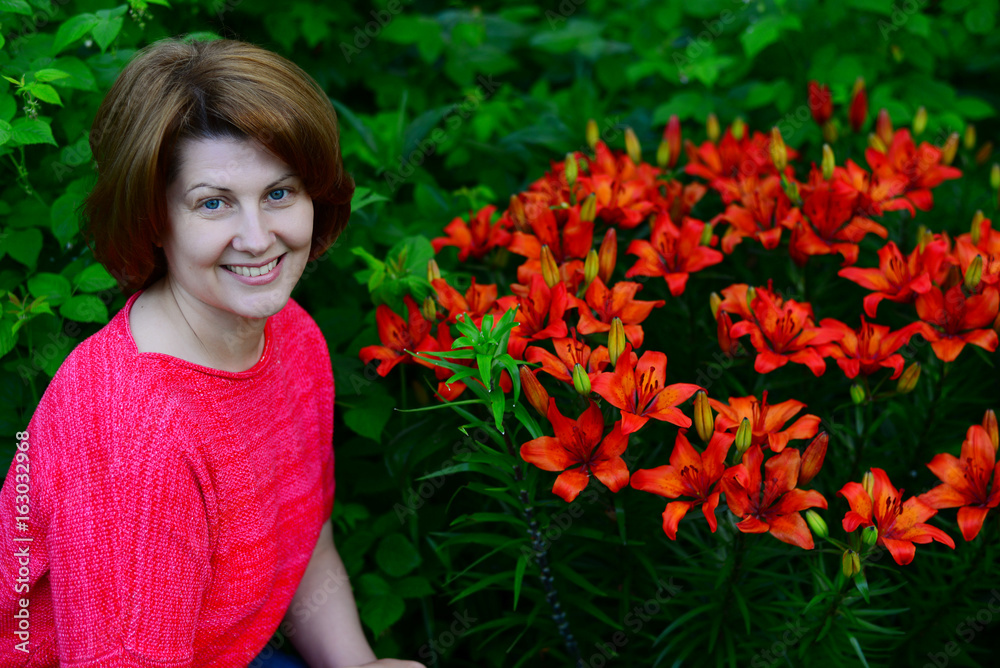Naklejka premium Woman near flower bed with orange lilies