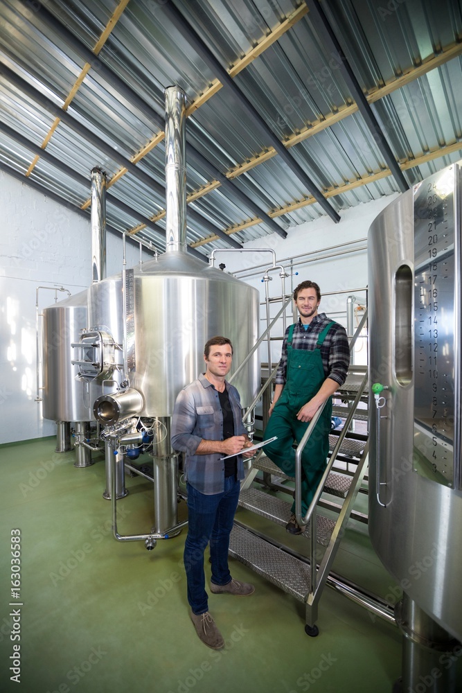 Coworkers standing by storage tank at brewery Coworkers standing by storage tank at brewery