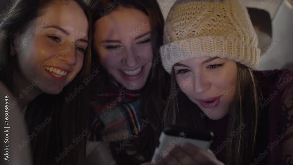 Closeup Of Happy Young Women Looking At Smart Phone Together In Backseat Of Moving Car In City Closeup Of Happy Young Women Looking At Smart Phone Together In Backseat Of Moving Car In City
