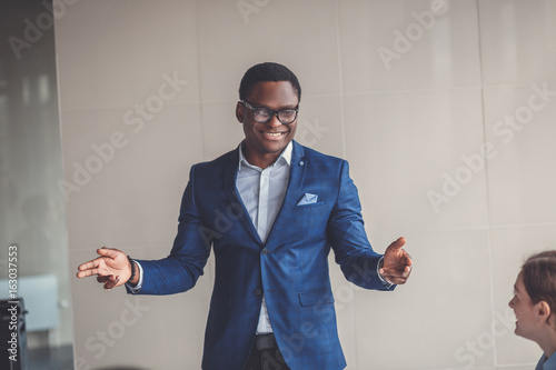 Portrait of smiling pretty young african business man in glasses sitting on workplace photo