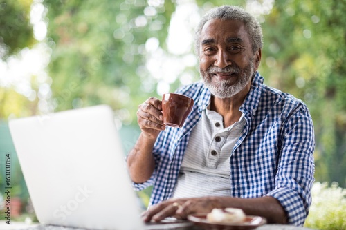 Portrait of man having coffee while using laptop
