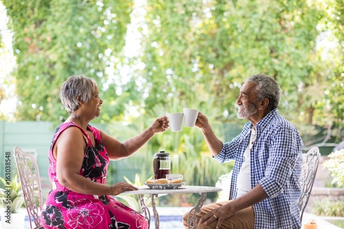 Smiling couple toasting coffee cups while sitting in yard photo