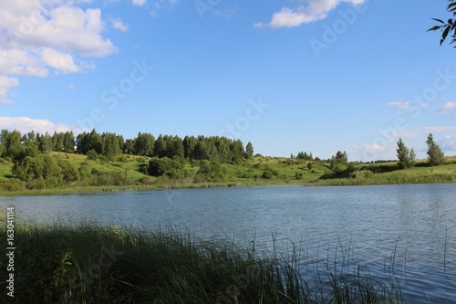 The lake is in good sunny weather. The water is riddled with a slight ripple. The shores of the lake are covered with luscious green vegetation.