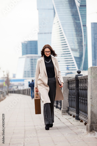 Fotografie Smiling dark-haired woman in a bright coat is on the waterfront
