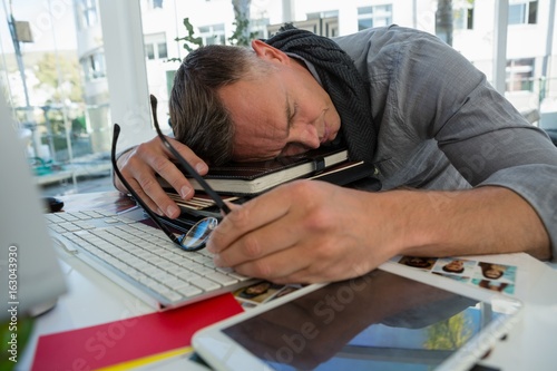 Tired businessman sleeping on files while sitting at desk