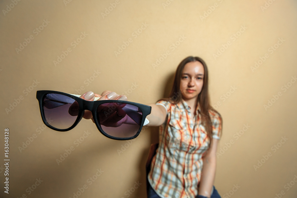 Fototapeta premium Emotional portrait of young cute white girl in plaid shirt with sunglasses opposite sienna background.