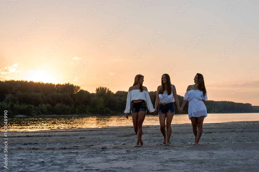 Fototapeta premium Three girls walking on the beach in the sunset