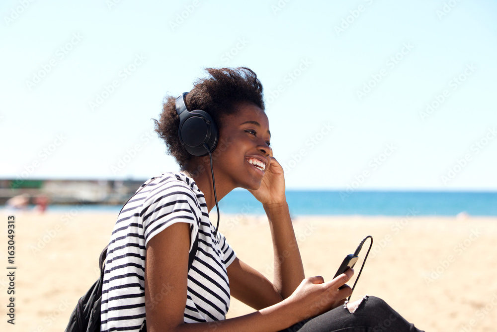 Smiling young woman sitting outdoors istening to music on headphones