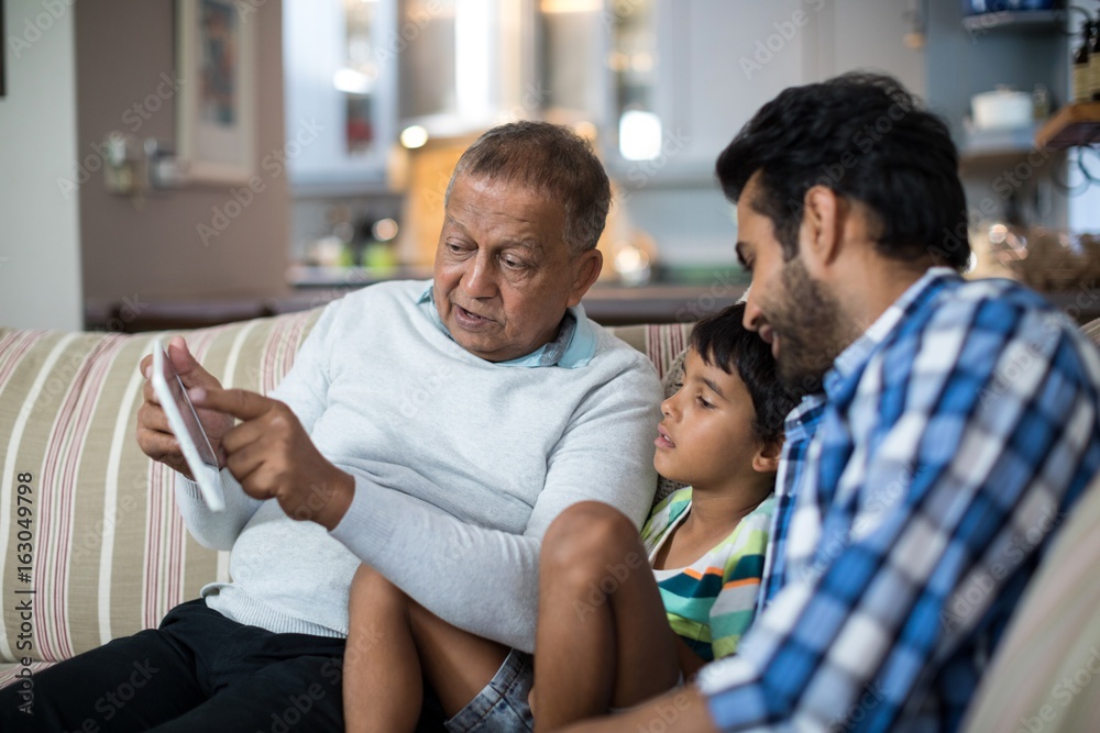 Fototapeta premium Grandfather showing tablet to grandson sitting with father at ho
