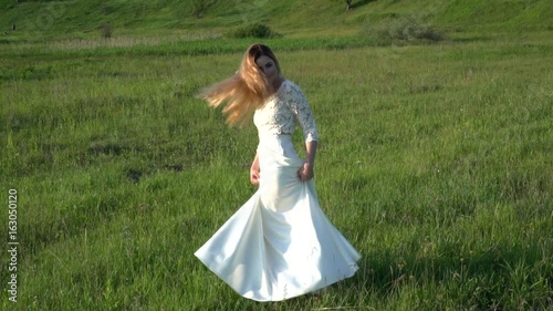 Beautiful young woman in white dress playing with hair on the meadow