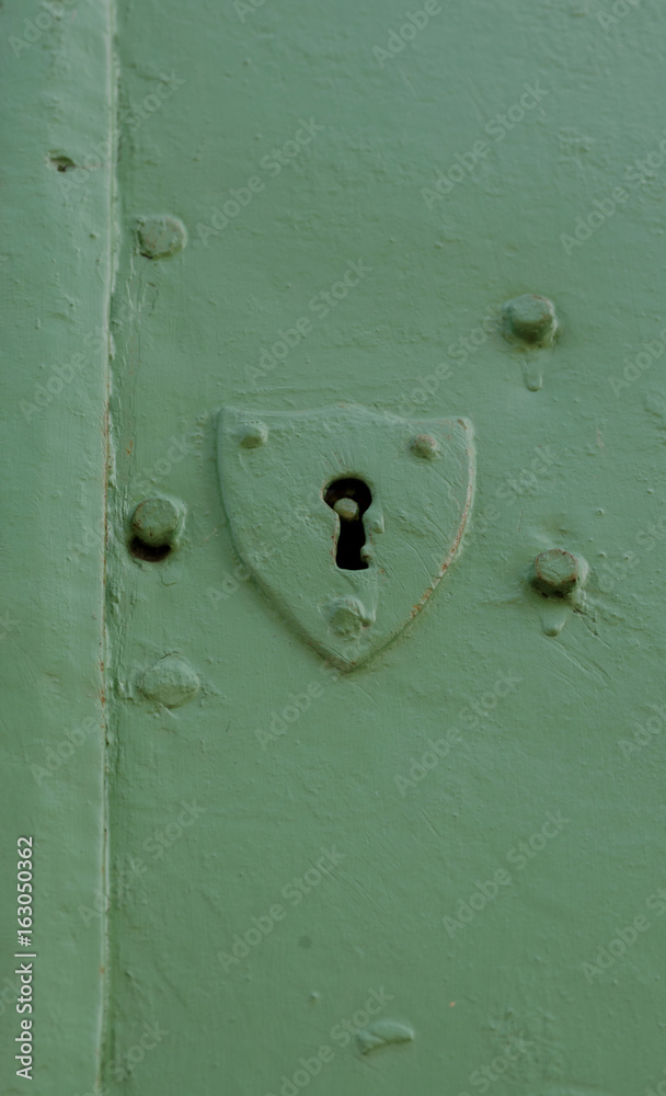 Old and plain shield shaped door key hole on a green door
