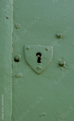 Old and plain shield shaped door key hole on a green door