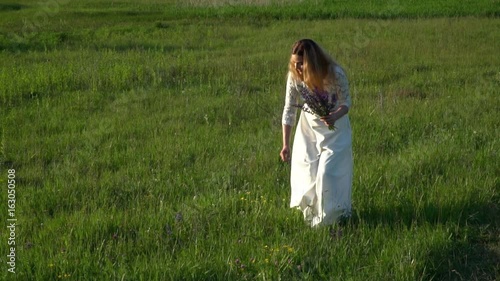 Beautiful young woman gathering flowers on the meadow