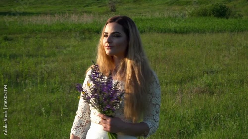 Beautiful young woman walking on the meadow with flowers closeup