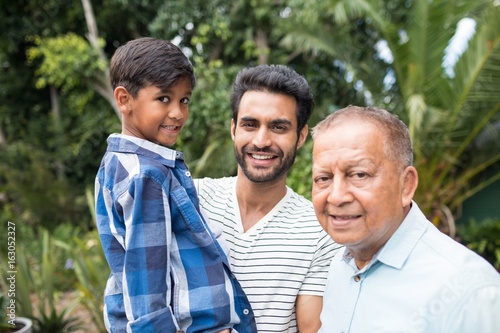 Portrait of father carrying son while standing by senior man