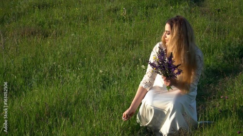 Beautiful young woman walking on the meadow with flowers on the sunset