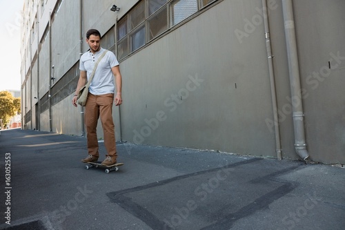 Young man skating on footpath by building
