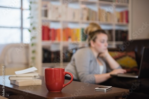 Books, mobile phone and coffee cup on table with woman in background photo
