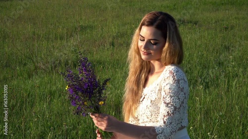 Beautiful young woman sitting on the meadow with flowers on the sunset closeup