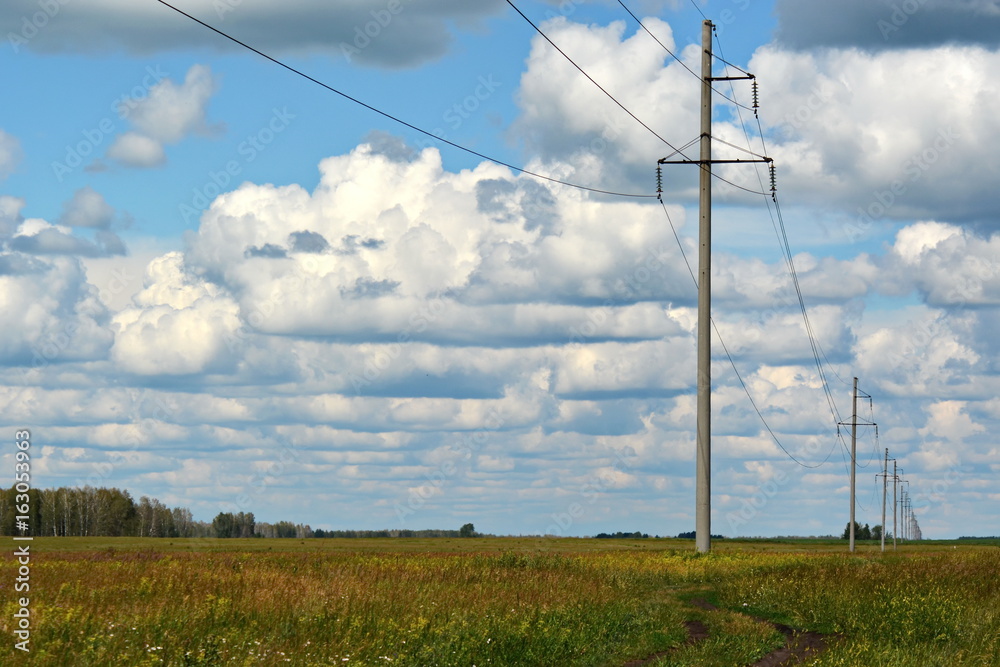 the electricity poles on the field outside of town, under a cloudy sky the electricity poles on the field outside of town, under a cloudy sky
