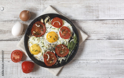 Fried eggs with vegetables and greens (tomatoes, onion, dill) on wooden background on a linen napkin with copy space for your text.