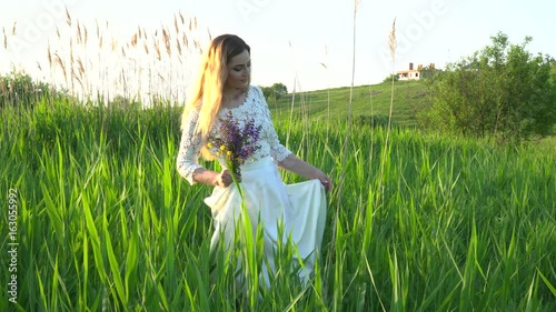 Beautiful woman in white dress walking in the grass on the meadow
