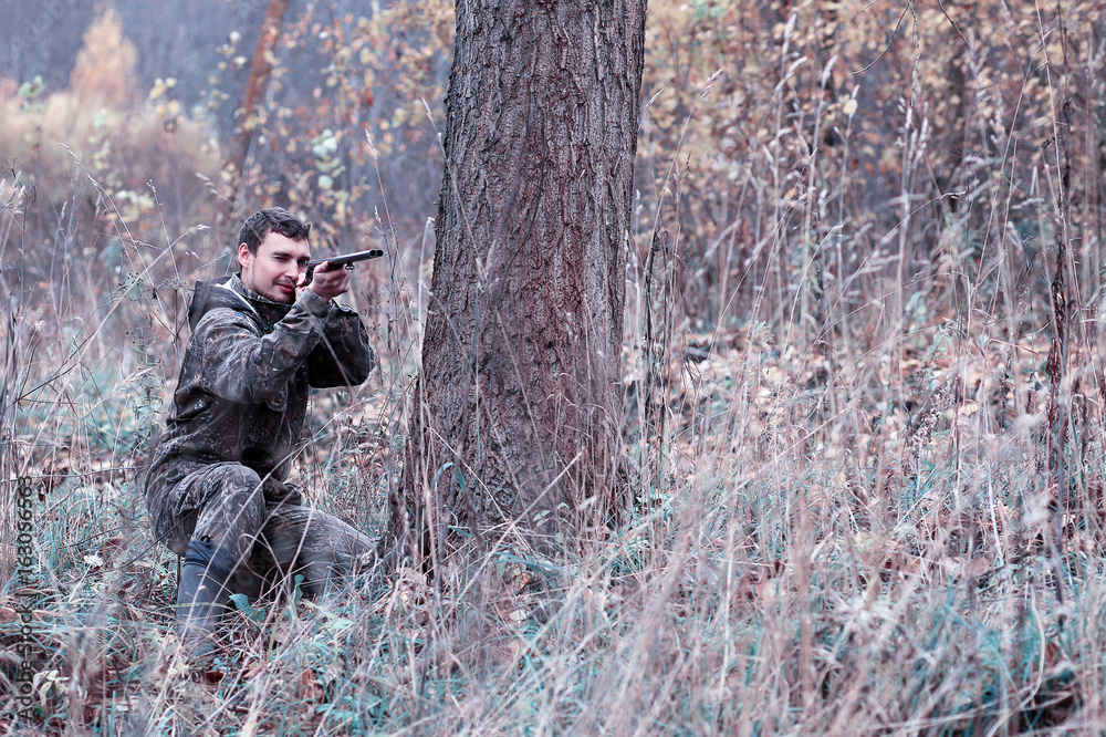 Fototapeta premium A man in camouflage and with a hunting rifle in a forest on a spring hunt