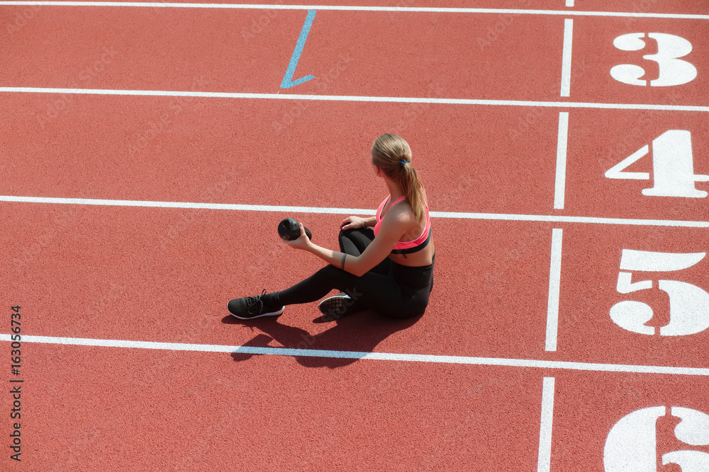 Obraz premium Young sporty woman athlete in sportswear sitting and keep shake with water on stadium track