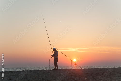 Fisherman standing on a pier at dawn sky background with sun rays and reflected in the sea water,Sunset fisherman