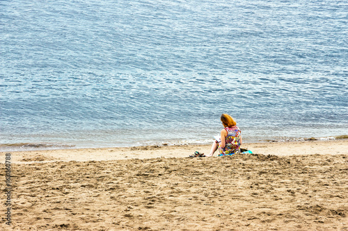 Lonely girl with red hair reading a book sitting on the beach