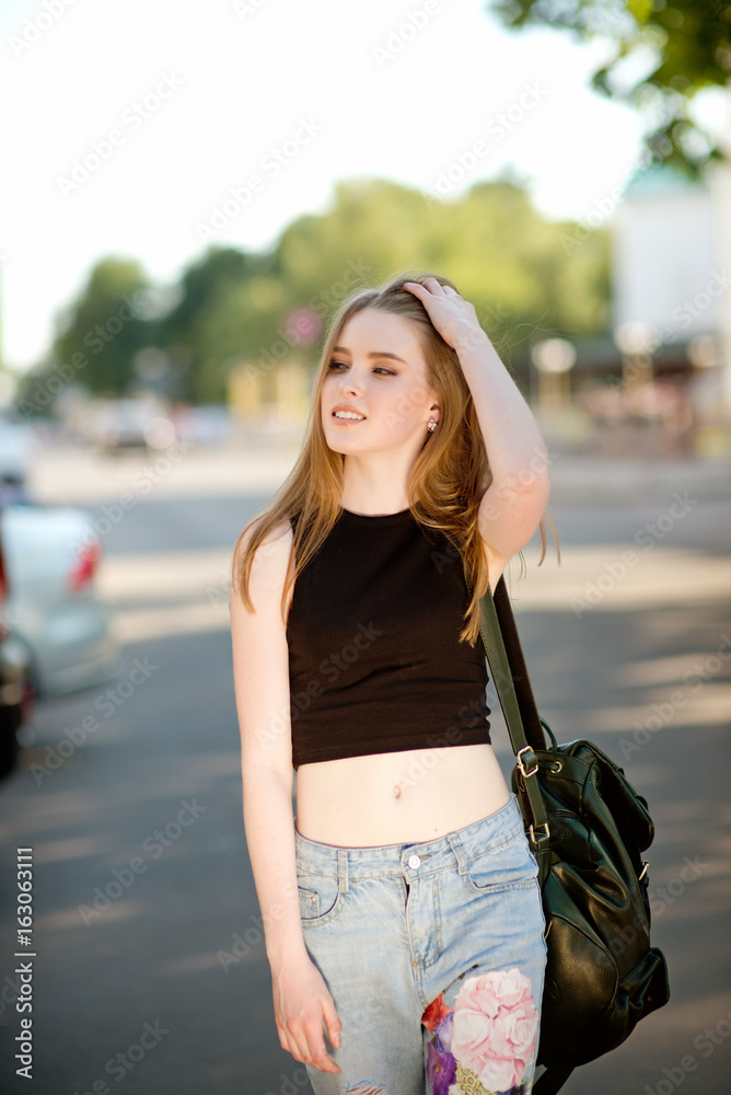 Obraz premium A beautiful young stylishly dressed girl walks in the city, drinks juice or a cocktail, eats sweets, makes selfie on a mobile phone