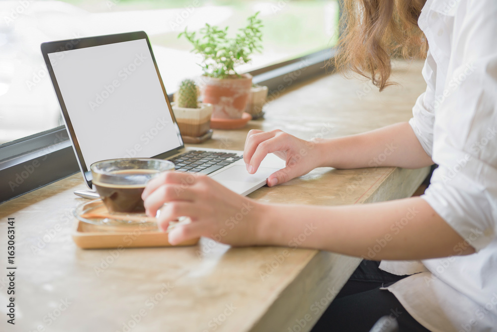 Girl using laptop and showing a blank screen sitting on a couch in the living room with glass of hot coffee at home with a warm light in the background Girl using laptop and showing a blank screen sitting on a couch in the living room with glass of hot coffee at home with a warm light in the background