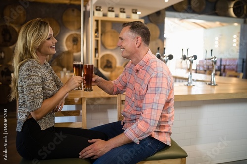 Photography Couple interacting while toasting a glass of beer at bar counter