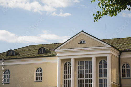 Close-up front wall of cottage house with gables and arched windows in sunlight. Nice sky with clouds
