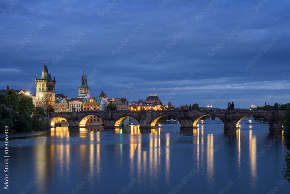 Lit Old Town Bridge Tower, other old buildings and Charles Bridge (Karluv most) and their reflections on the Vltava River in Prague, Czech Republic, at dusk. Copy space.