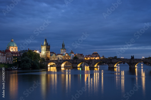 Lit Charles Bridge (Karluv most) and old buildings at the Old Town and their reflections on the Vltava River in Prague, Czech Republic, at dusk. Copy space.