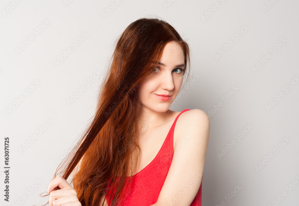 Portrait of a beautiful young woman holding a strand of her red ginger long shiny hair Portrait of a beautiful young woman holding a strand of her red ginger long shiny hair