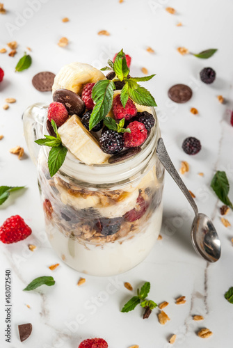 Summer fruit berry breakfast. Healthy banana split breakfast with cream cheese, raspberries, blackberries, mint, white and pink chocolate. In mason jar, marble table. Copy space