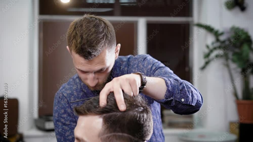 Man standing in salon and cutting hair to client sitting in chair Man standing in salon and cutting hair to client sitting in chair