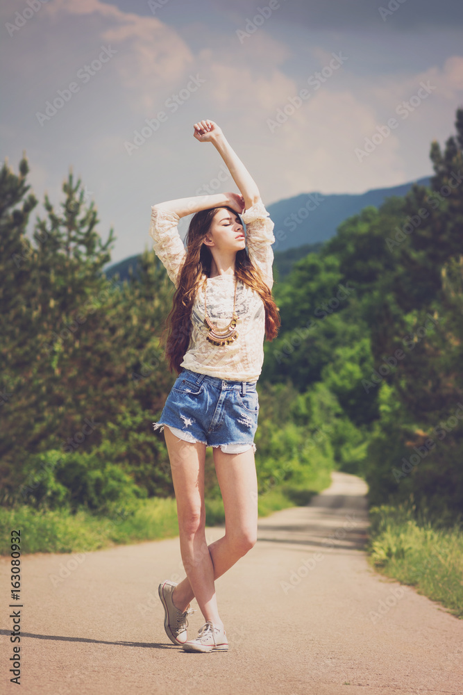 Modern young woman in denim shorts and lace top posing outdoor on the road in summer