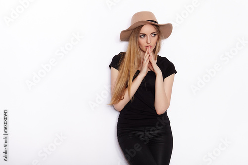 Young beautiful fashion model in women black t-shirt trendy hat black torn jeans posing in studio against white background